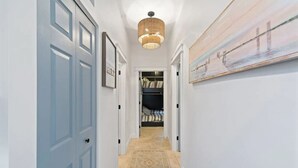 A hallway with a patterned rug, a hanging light fixture, and a painting on the wall. - Margate Home w/ Large Outdoor Kitchen (Margate City)