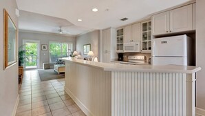 A kitchen with white cabinetry, a central island, and a refrigerator. - Shorenugh - Bright Villa with Rooftop Pool Next to Coligny Plaza by RedAwning (Hilton Head Island)