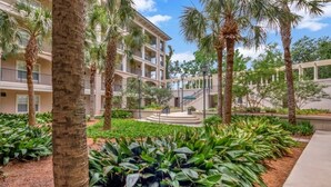 A multi-story building with balconies, surrounded by palm trees and lush greenery. - Shorenugh - Bright Villa with Rooftop Pool Next to Coligny Plaza by RedAwning (Hilton Head Island)
