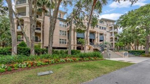 A multi-story residential building with balconies, a central staircase, and a well-maintained garden area. - Shorenugh - Bright Villa with Rooftop Pool Next to Coligny Plaza by RedAwning (Hilton Head Island)