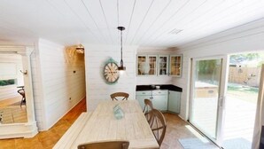 Een ruime eethoek met een houten tafel en stoelen, een hanglamp en uitzicht op de achtertuin door glazen deuren.