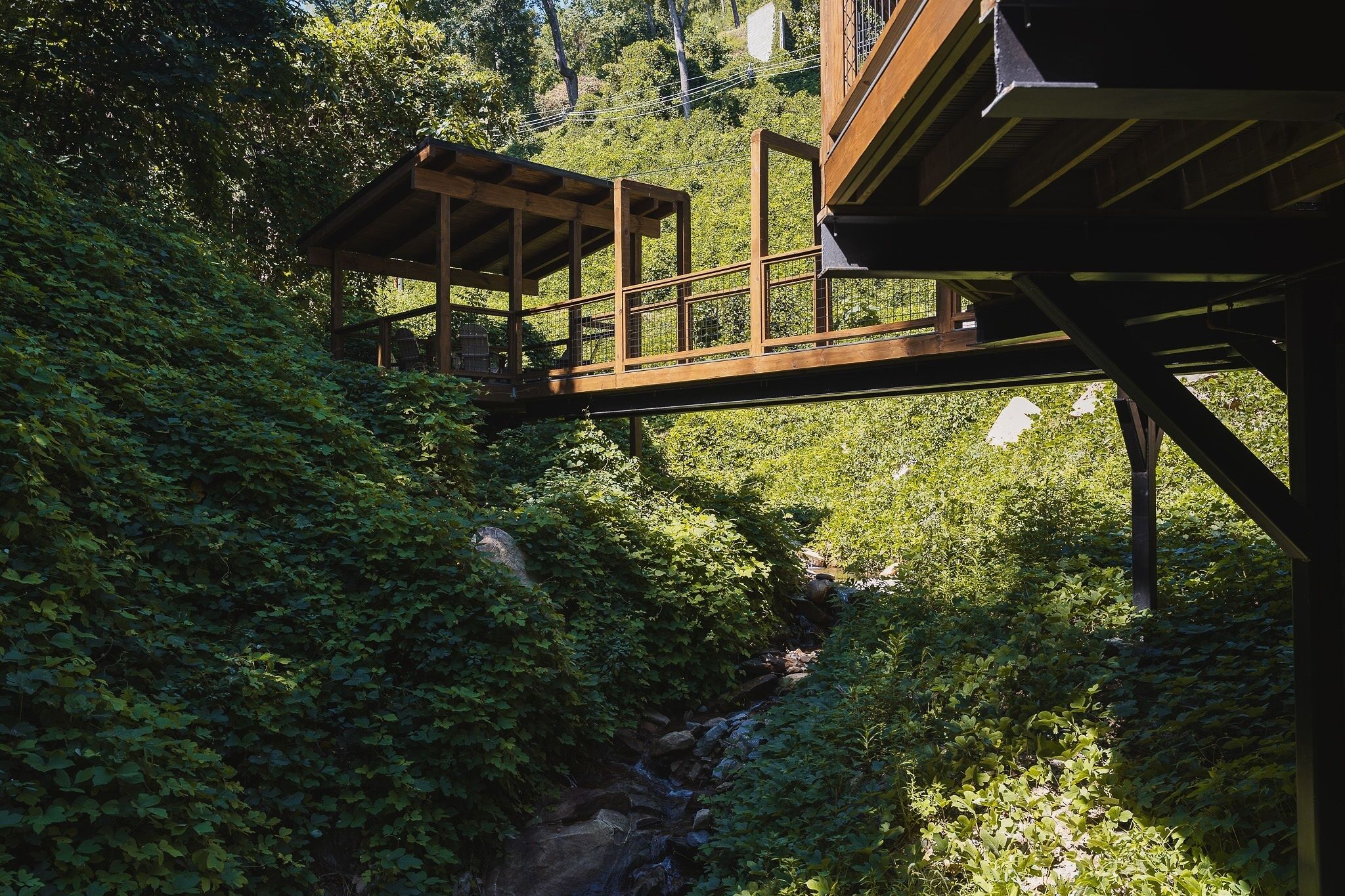 A wooden bridge connecting a building to a lush green area with a stream.