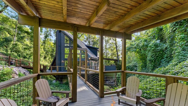 A wooden deck with Adirondack chairs, a fire pit, and a view of a house with a sloped roof. - Night Owl 3 Bedroom Cabin by RedAwning (Gatlinburg)