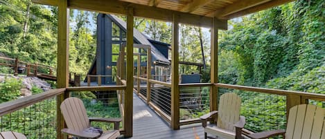 Una terraza de madera con sillas Adirondack, una fogata y vista a una casa con techo inclinado.