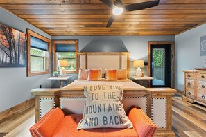 A bedroom with a wooden ceiling, a bed with multiple pillows, a nightstand with a lamp, and a dresser. - Night Owl 3 Bedroom Cabin by RedAwning (Gatlinburg)