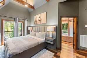 A bedroom with a large bed, a nightstand, a wall-mounted lamp, and a view of the outdoors through a window. - Night Owl 3 Bedroom Cabin by RedAwning (Gatlinburg)