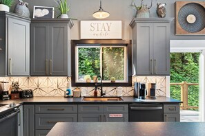 A modern kitchen with grey cabinets, a window with a view of greenery, a 'STAY' sign, and a fire extinguisher sign. - Night Owl 3 Bedroom Cabin by RedAwning (Gatlinburg)