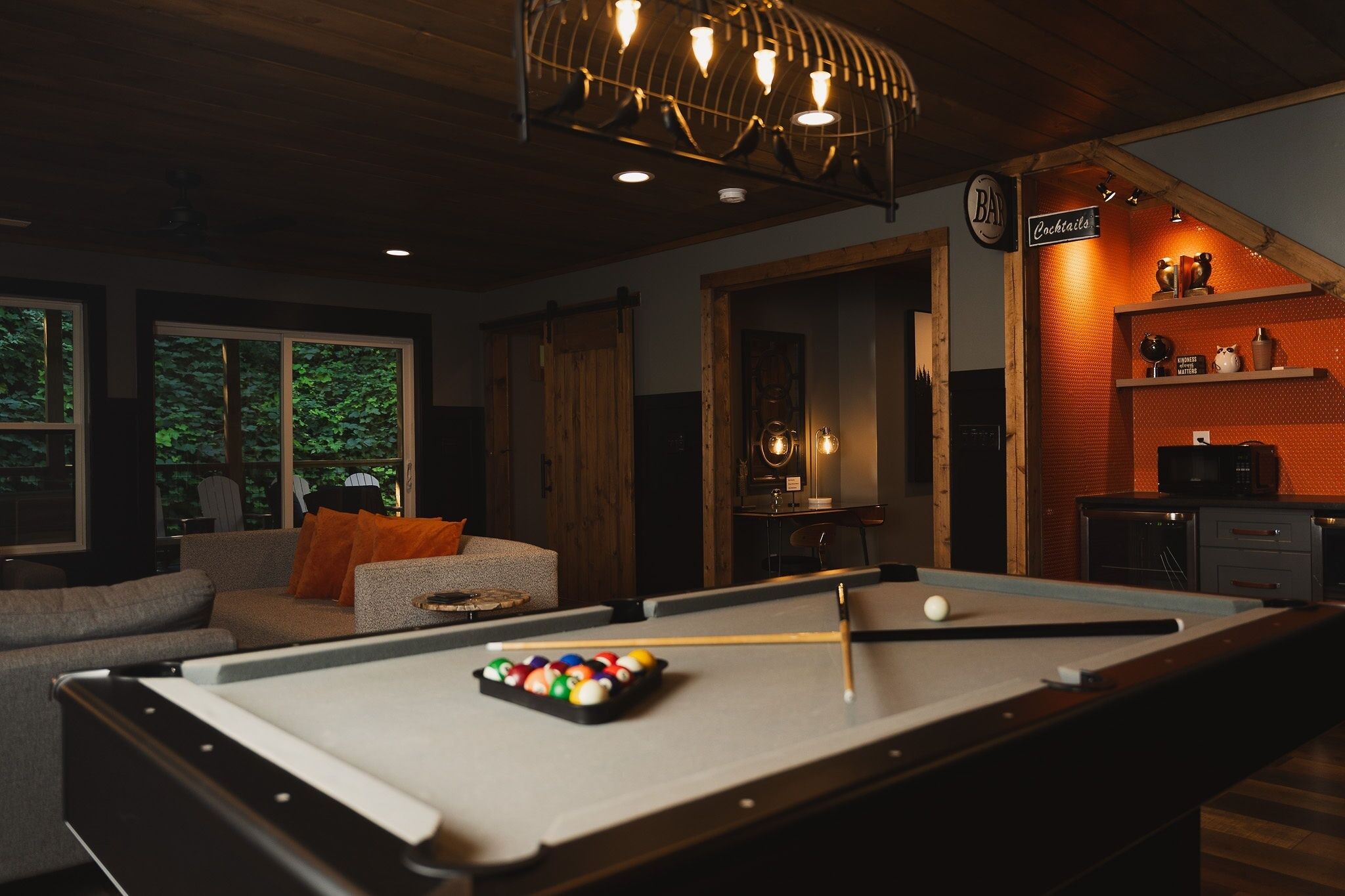 A pool table with balls, a sofa, and a bar area with a sign.