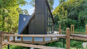 A modern house with a steep roof, large windows, and a wooden deck. - Night Owl 3 Bedroom Cabin by RedAwning (Gatlinburg)