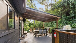 A covered outdoor deck with a table and chairs, a fire extinguisher, and a grill. - Night Owl 3 Bedroom Cabin by RedAwning (Gatlinburg)