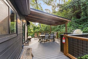 A covered outdoor deck with a table and chairs, a fire extinguisher, and a grill. - Night Owl 3 Bedroom Cabin by RedAwning (Gatlinburg)