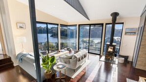 Ein modernes Wohnzimmer mit großem Fenster mit Seeblick, Kamin und gemütlicher Sitzecke.