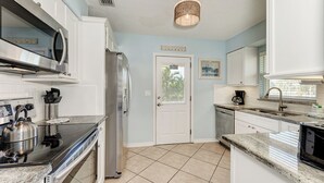 A modern kitchen with white cabinets, stainless steel appliances, a granite countertop, and a tiled floor. - Casa Sierra 203B - 2BR Condo with Pool - By Island Real Estate Vacations (Holmes Beach)