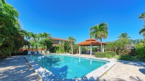 A swimming pool with a tiled deck, surrounded by palm trees and a gazebo. - Casa Sierra 203B - 2BR Condo with Pool - By Island Real Estate Vacations (Holmes Beach)