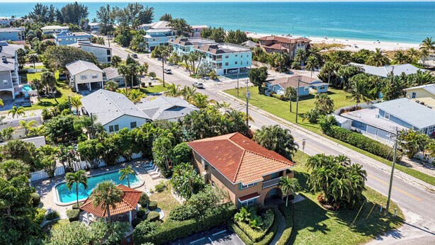An aerial view of a coastal residential area with houses, a swimming pool, and a beach in the background. - Casa Sierra 203B - 2BR Condo with Pool - By Island Real Estate Vacations (Holmes Beach)