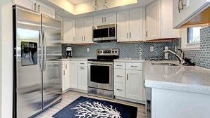 A modern kitchen with stainless steel appliances, white cabinets, and a black backsplash. - Sugaree -  2bedroom Private Pool Property in Holmes Beach (Holmes Beach)