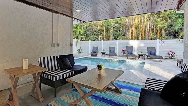 A modern outdoor lounge area with a pool, wooden furniture, and a view of bamboo trees. - Sugaree -  2bedroom Private Pool Property in Holmes Beach (Holmes Beach)