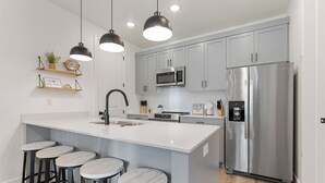 A modern kitchen with a central island, stainless steel appliances, and bar stools. - Holiday House #73: Desert Color Lagoon + Beaches (St. George)