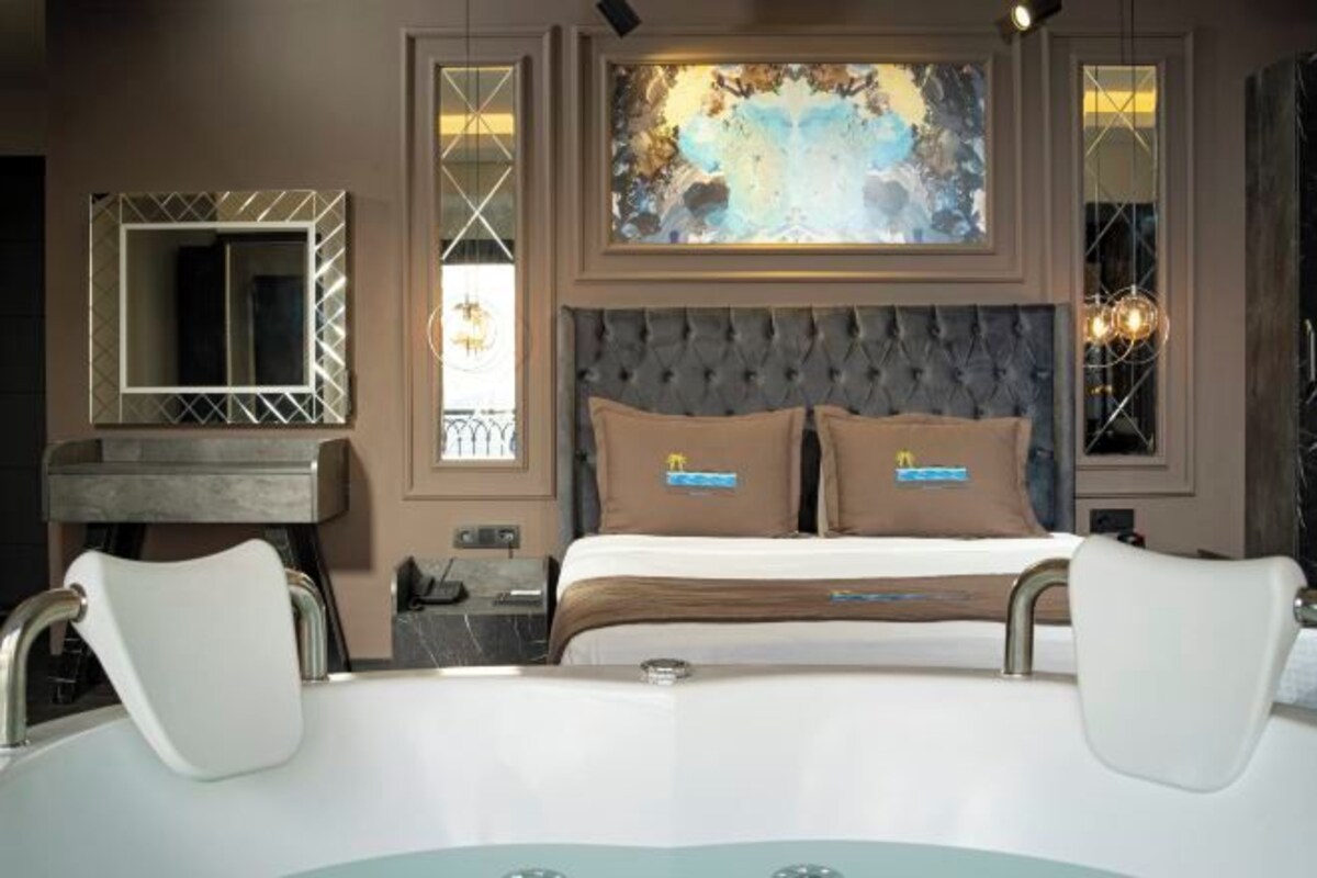 A modern hotel room with a large bed, a vanity with a mirror, and a painting above the bed.