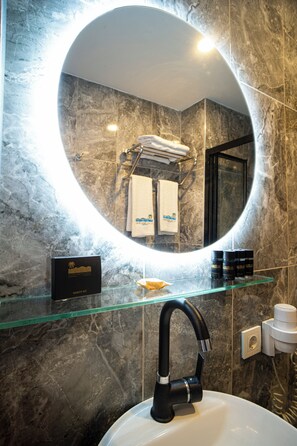 A bathroom with a round mirror, a black faucet, a glass shelf with toiletries, and a marble wall.