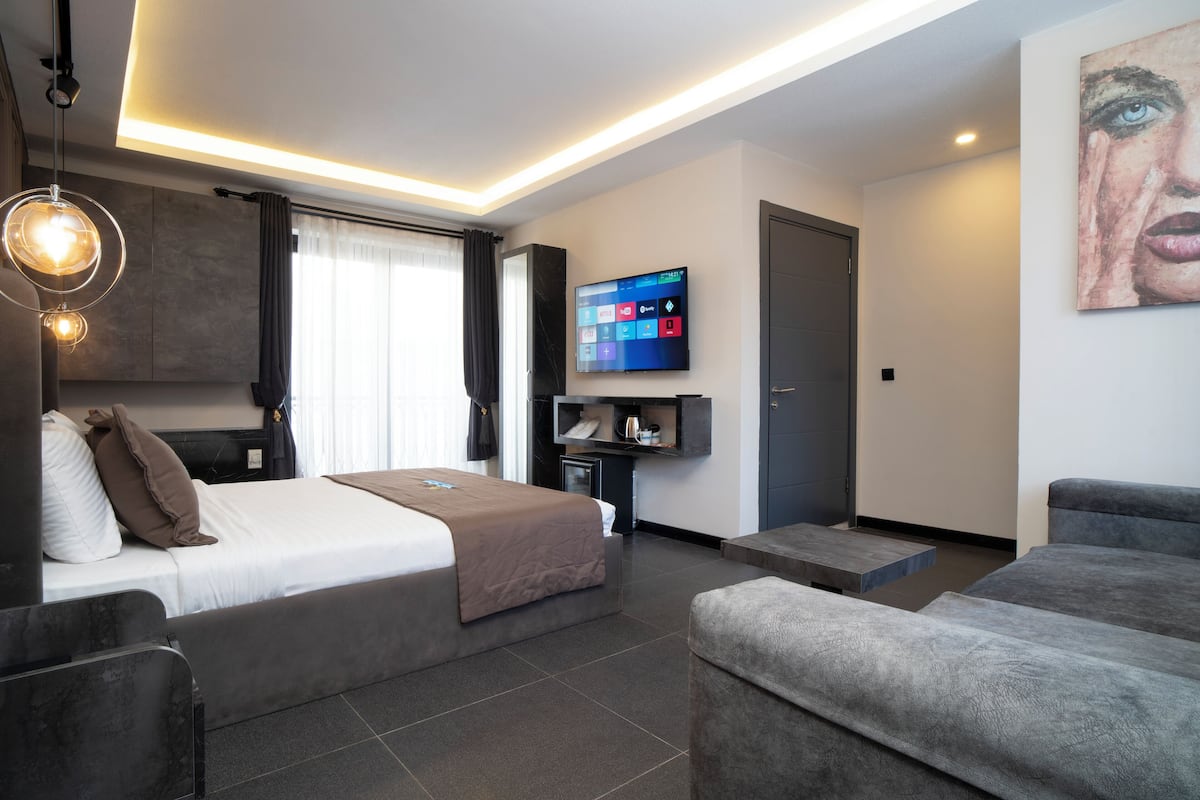 Moderni hotellihuone, jossa on sänky, sohva, televisio ja taideteos seinällä.