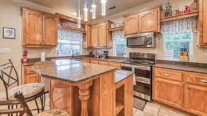 A kitchen with wooden cabinets, granite countertops, stainless steel appliances, and pendant lighting.