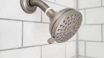 A showerhead with a round, perforated design mounted on a wall with white tiles.