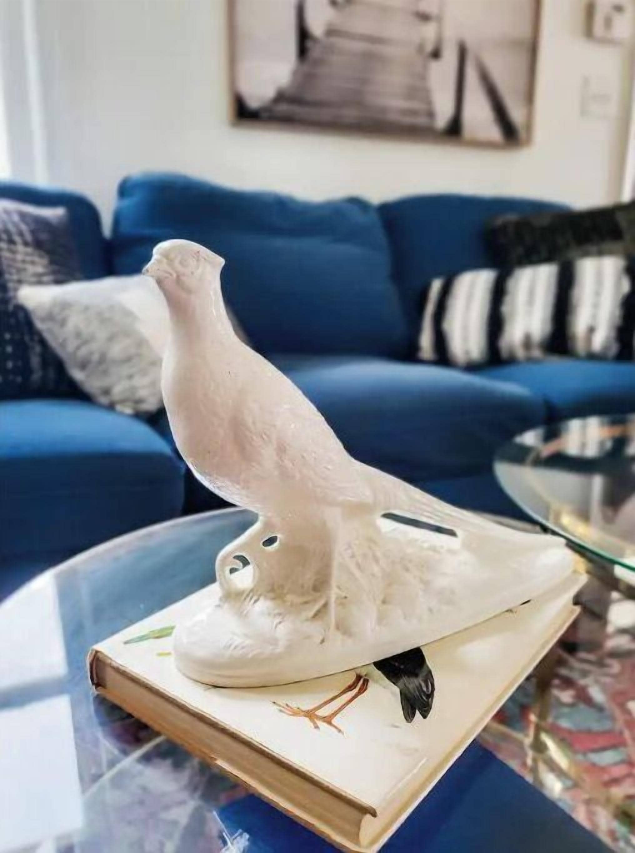 Une statuette d’oiseau blanc posée sur un livre, un canapé bleu et un tapis à motifs dans un salon.