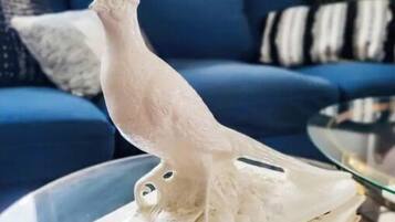 Une statuette d’oiseau blanc posée sur un livre, un canapé bleu et un tapis à motifs dans un salon.