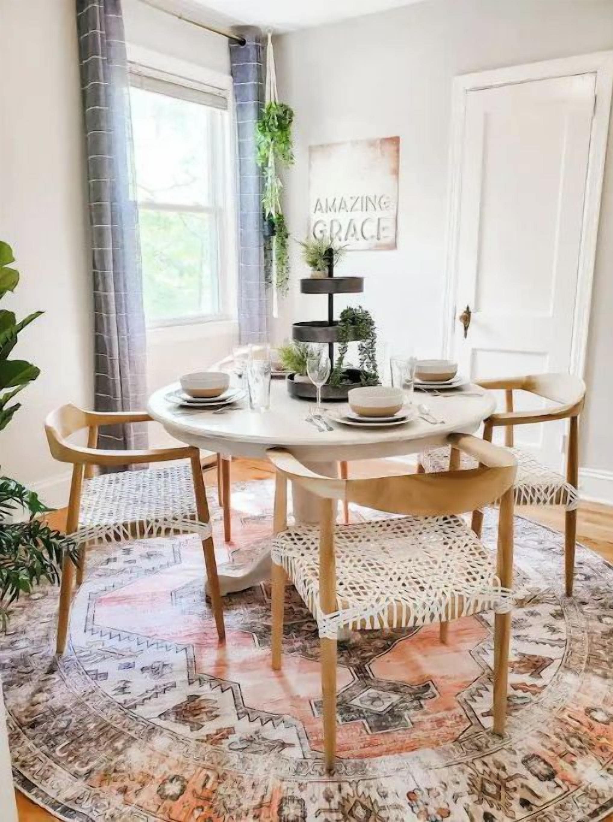 A dining area with a round table, four chairs, a patterned rug, and a wall-mounted plant.