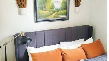 Un dormitorio con cama, almohadas, una mesita de noche, una lámpara y un cuadro en la pared.