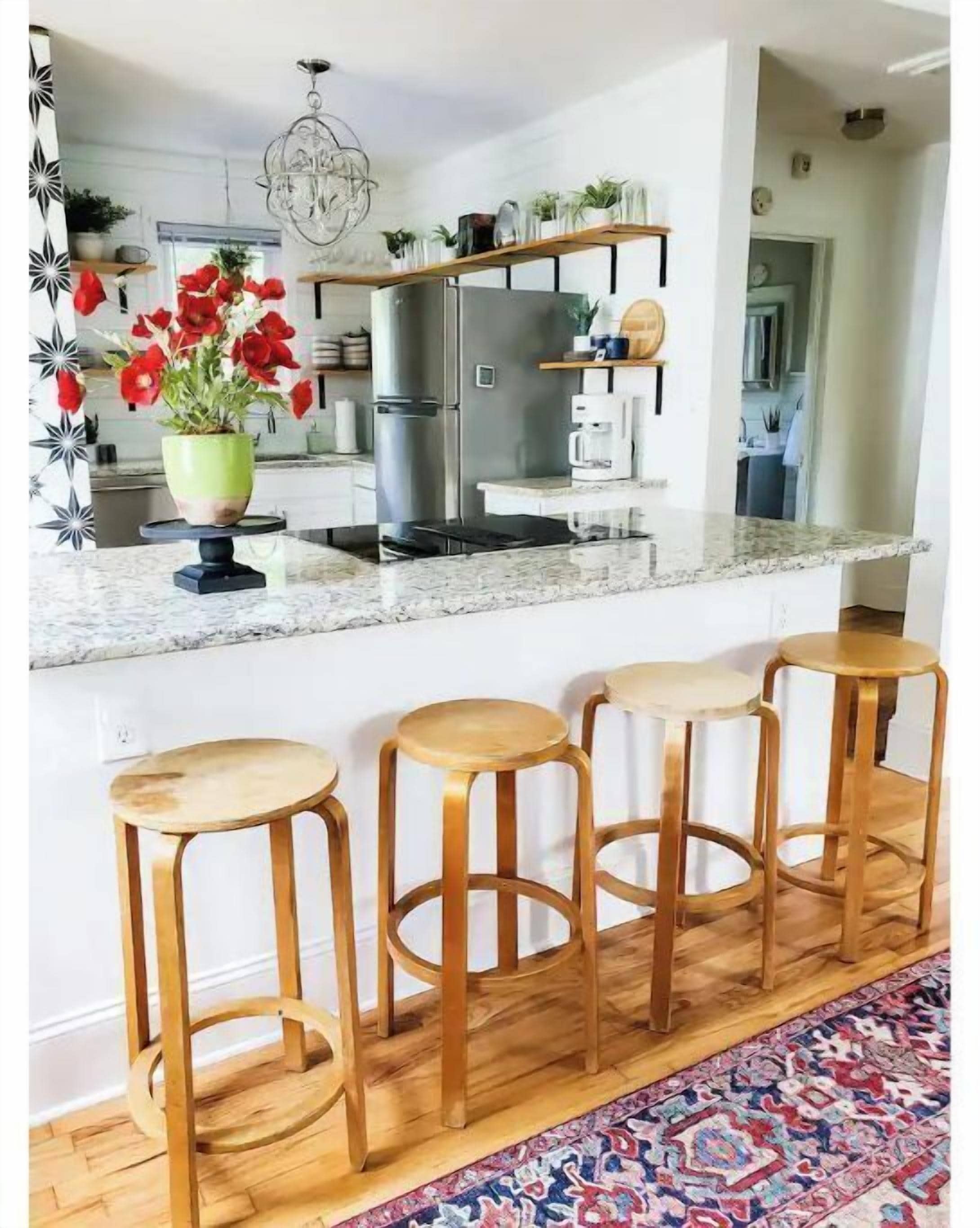 A modern kitchen with a marble countertop, stainless steel appliances, and wooden stools.