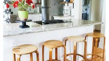 A modern kitchen with a marble countertop, stainless steel appliances, and wooden stools.