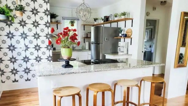 A kitchen with a central island, bar stools, a refrigerator, and a hanging plant. - The Haymount Eclectic by Haymount Homes (Fayetteville)