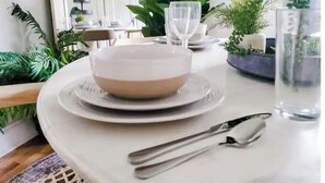 A dining table set with plates, bowls, cutlery, and glasses, surrounded by potted plants. - The Haymount Eclectic by Haymount Homes (Fayetteville)