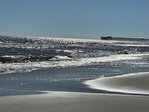 Una playa con olas y un muelle al fondo.