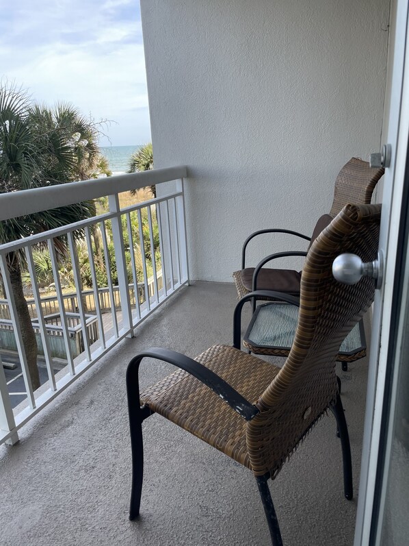 En fletstol med metalstel på en balkon med gelænder, der udover en strand og palmer.
