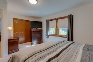 Un dormitorio con cama, cómoda, televisión y ventana con cortinas.