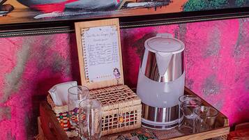 Una habitación con un cuadro de una escena de playa, una bandeja de madera con vasos y un menú, y un refrigerador.