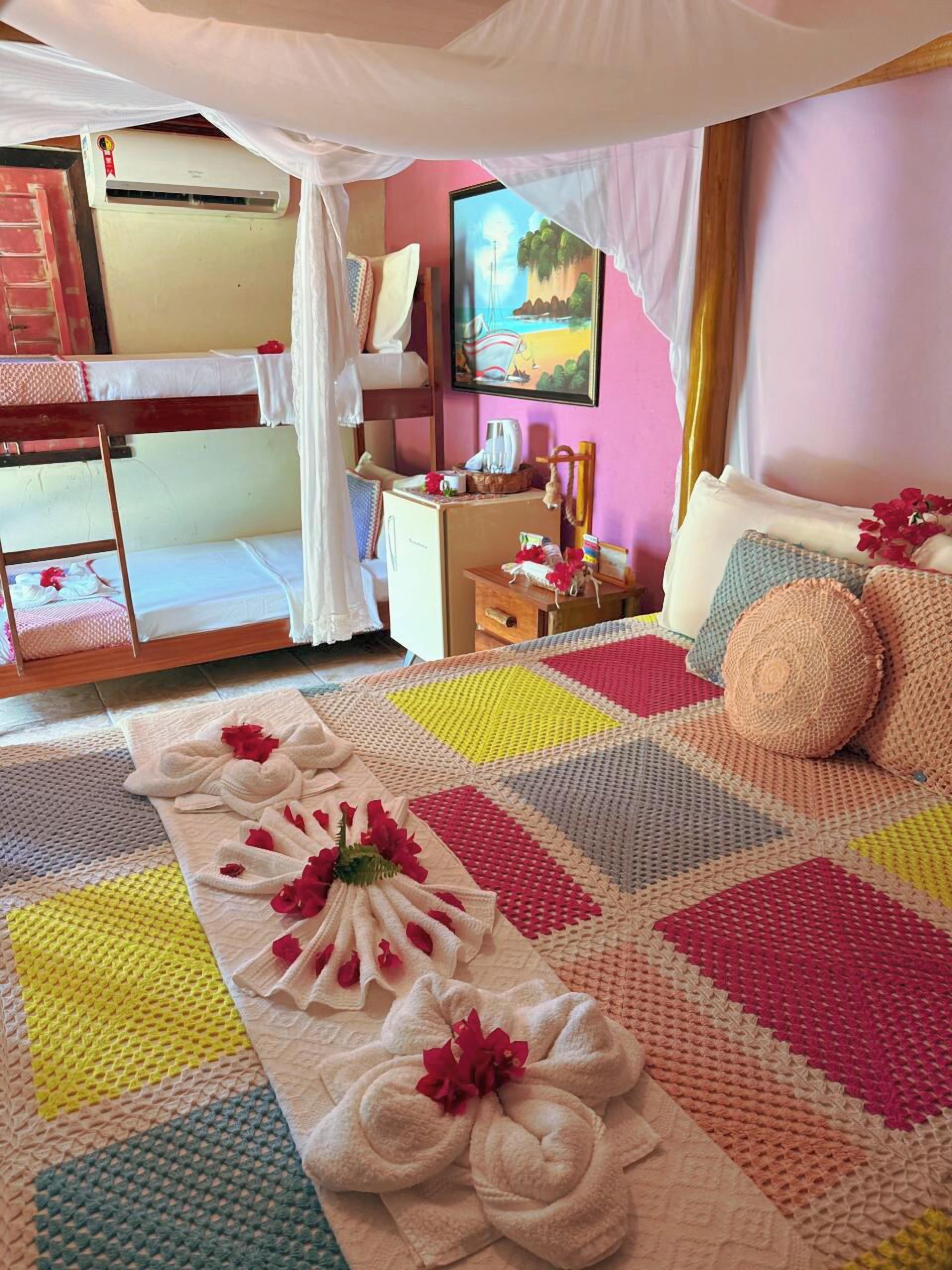 A hotel room with bunk beds, a bedside table with a lamp, a painting on the wall, and a colorful blanket on the bed.