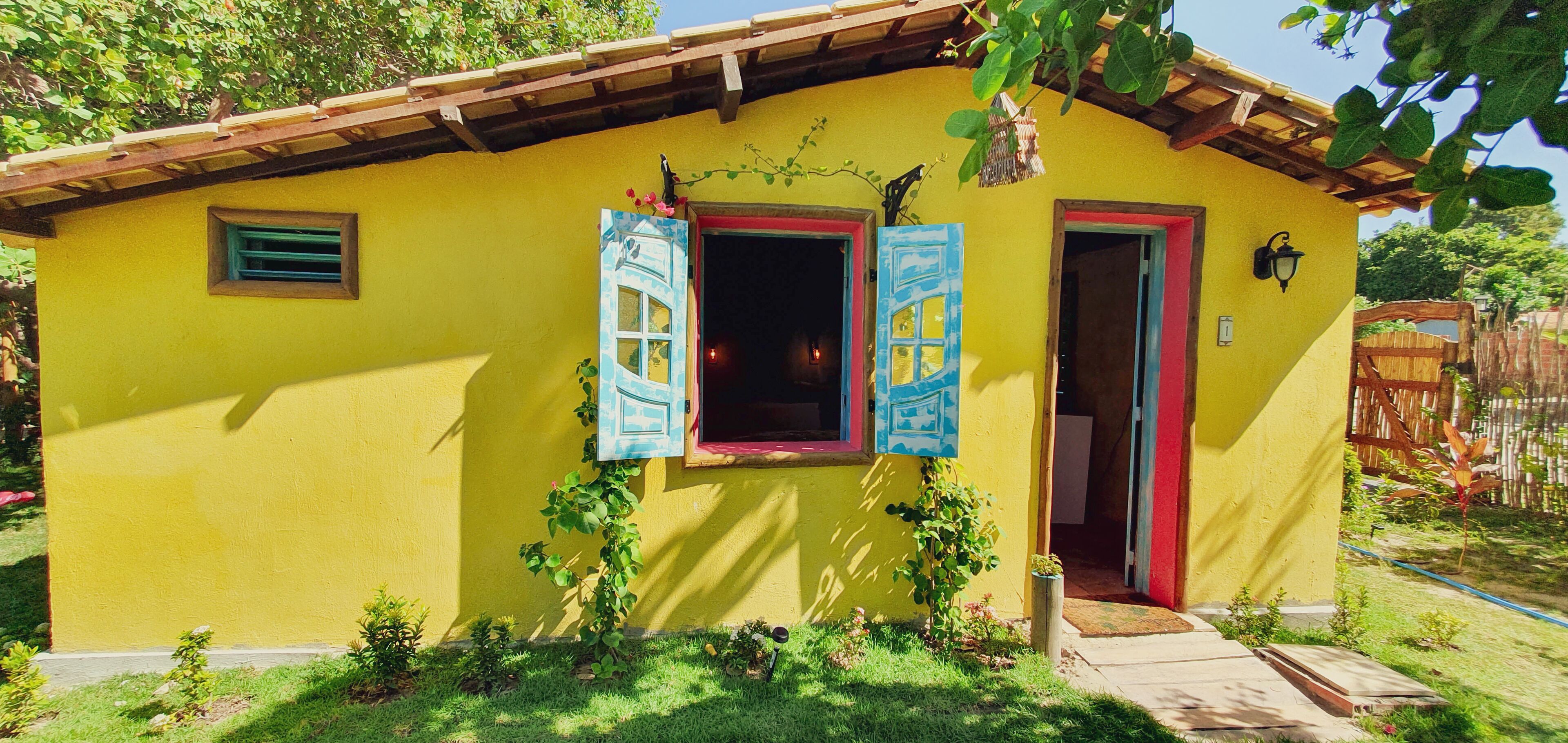 A yellow building with two doors and windows, surrounded by greenery.