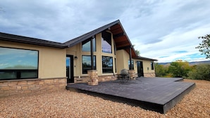 Une maison moderne dotée d’une grande terrasse, de fondations en pierre et de larges fenêtres.