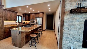 Une cuisine moderne avec des meubles en bois, un plan de travail en granit et un îlot central intégré, agrémenté de tabourets de bar.