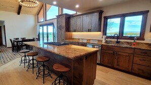 Une cuisine moderne avec des meubles en bois, un plan de travail en granit et un coin bar avec des tabourets.