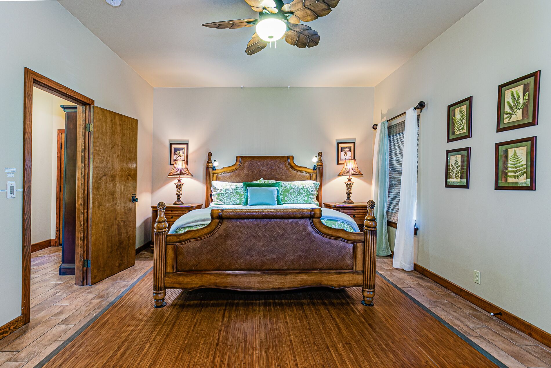 A bedroom with a wooden bed, two bedside lamps, and framed botanical prints on the wall.