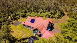 A modern house with a red roof, surrounded by dense forest. - Dancing Ferns in Volcano, Hawaii (Volcano)