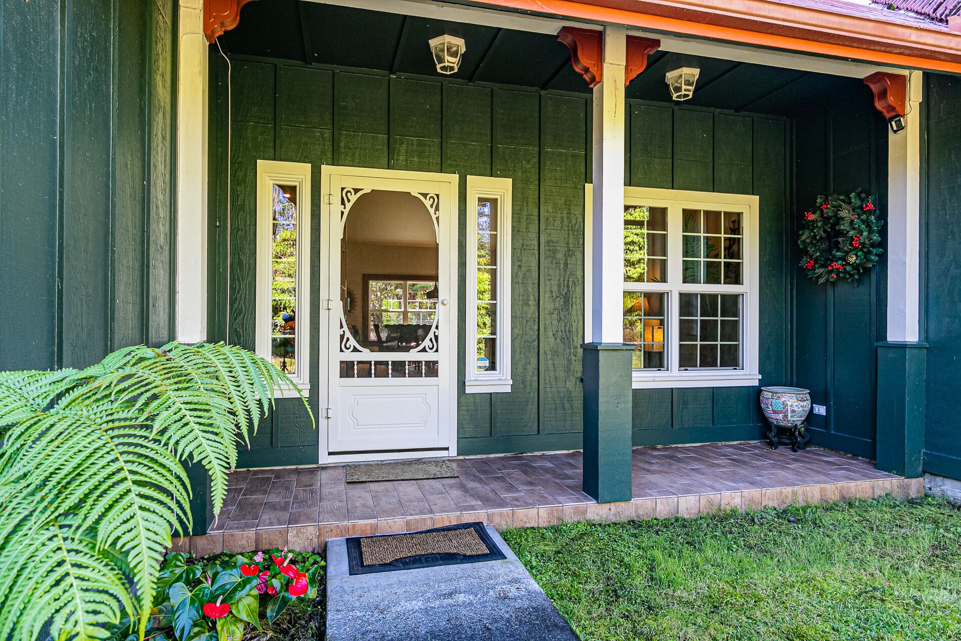 A green house with a white door and windows, a porch with a bench, and a potted plant.