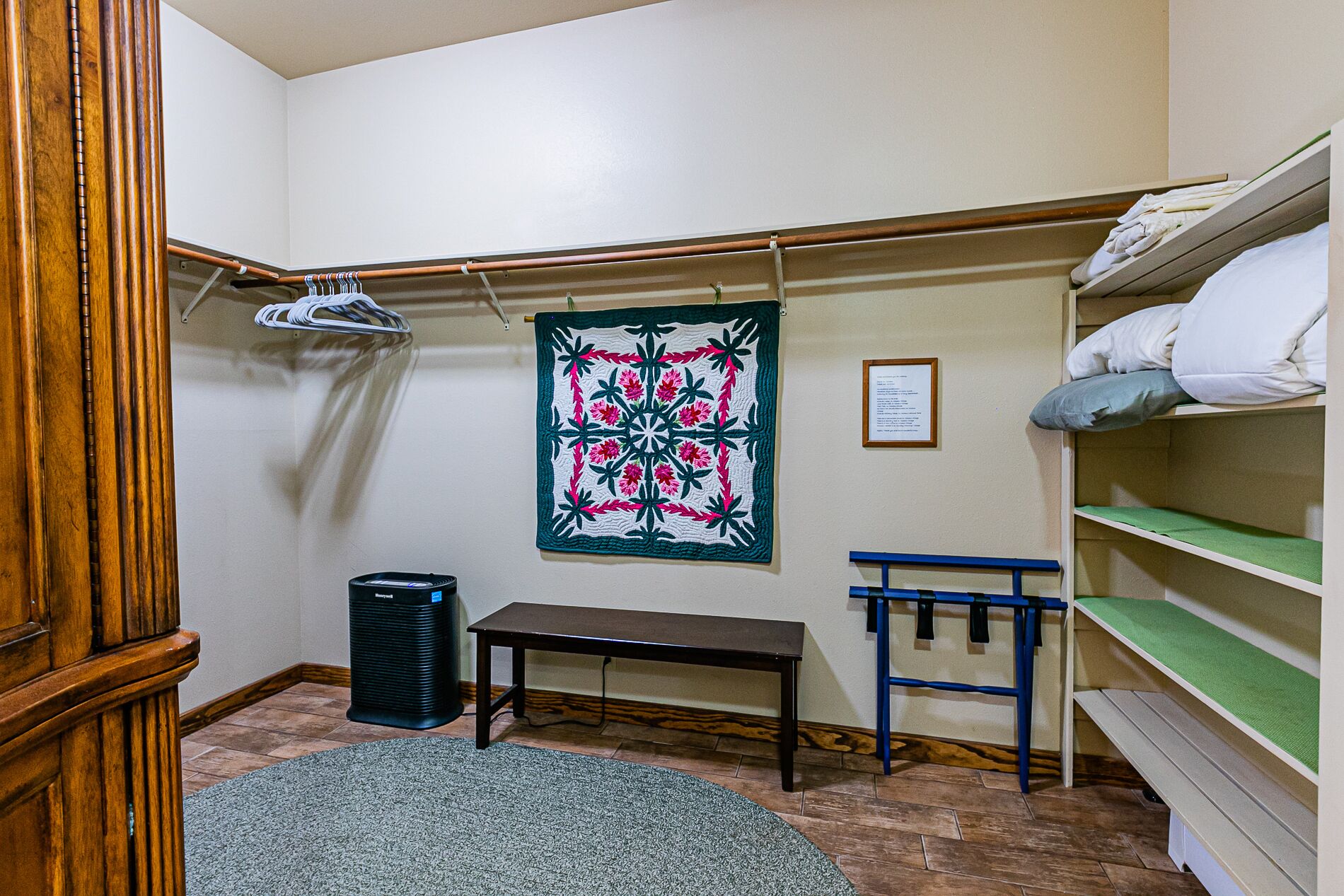 A room with a bench, a hanging laundry rack, a trash can, and a bunk bed with a green mattress.