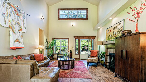A spacious living room with a high ceiling, a fireplace, and a large window overlooking a garden. - Dancing Ferns in Volcano, Hawaii (Volcano)