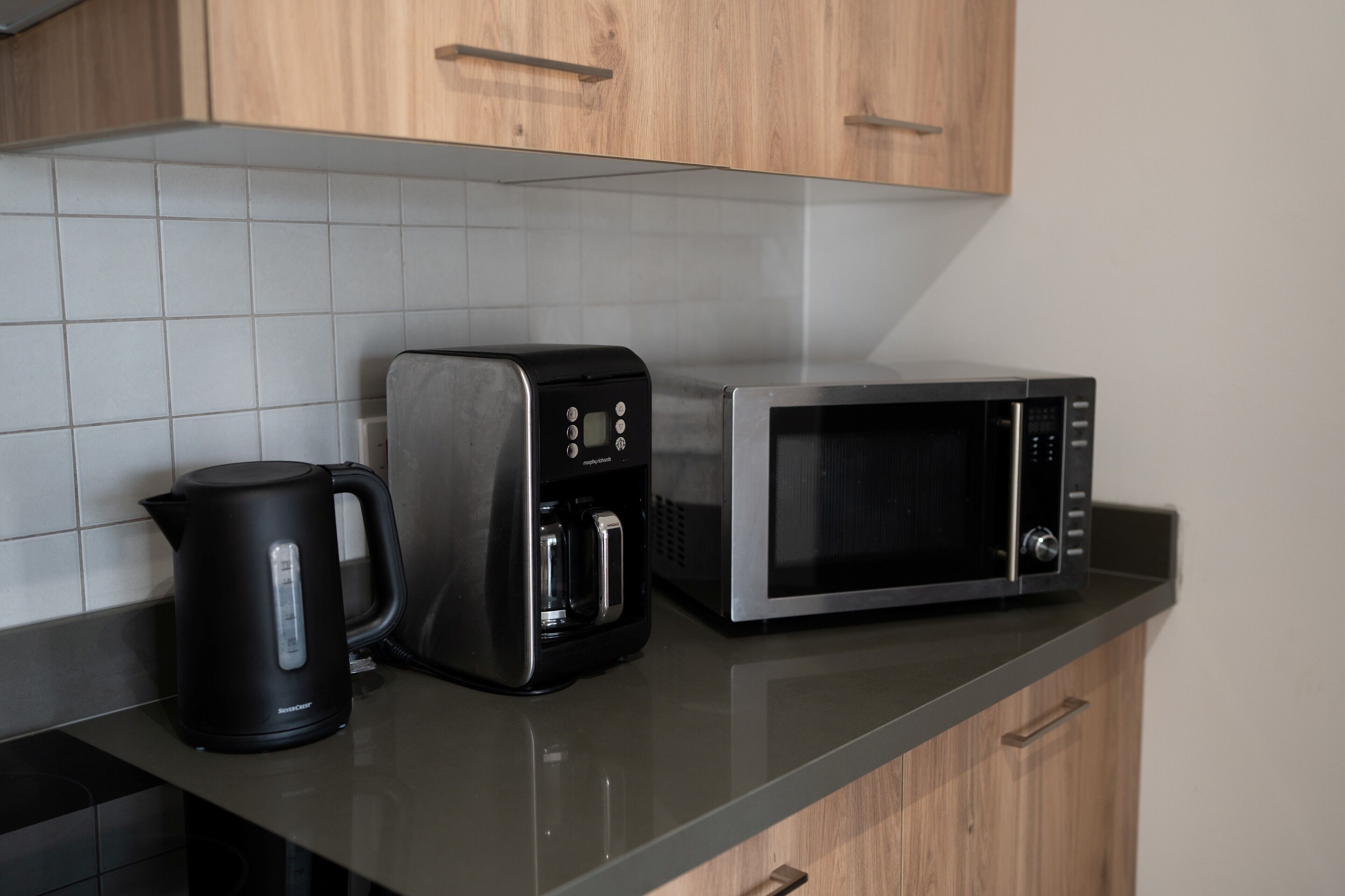 Una cocina con tetera, cafetera y microondas sobre una encimera.